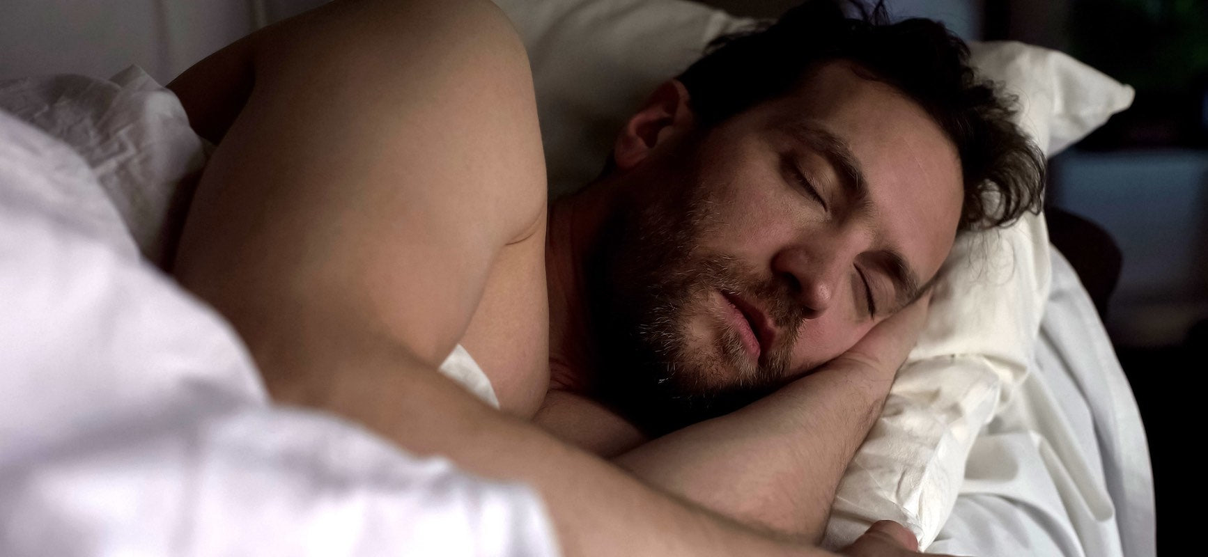 A bearded young man sleeps peacefully on his side