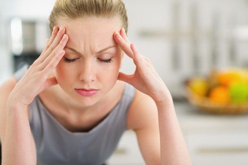 nicely dressed woman grimacing and holding her head in pain