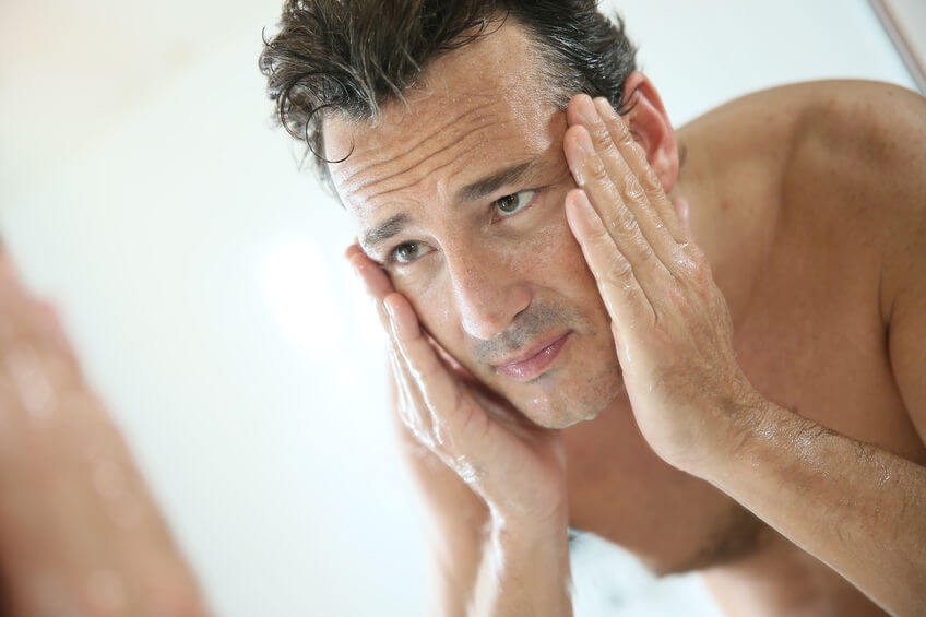 man gripping his face while observing intently in the mirror